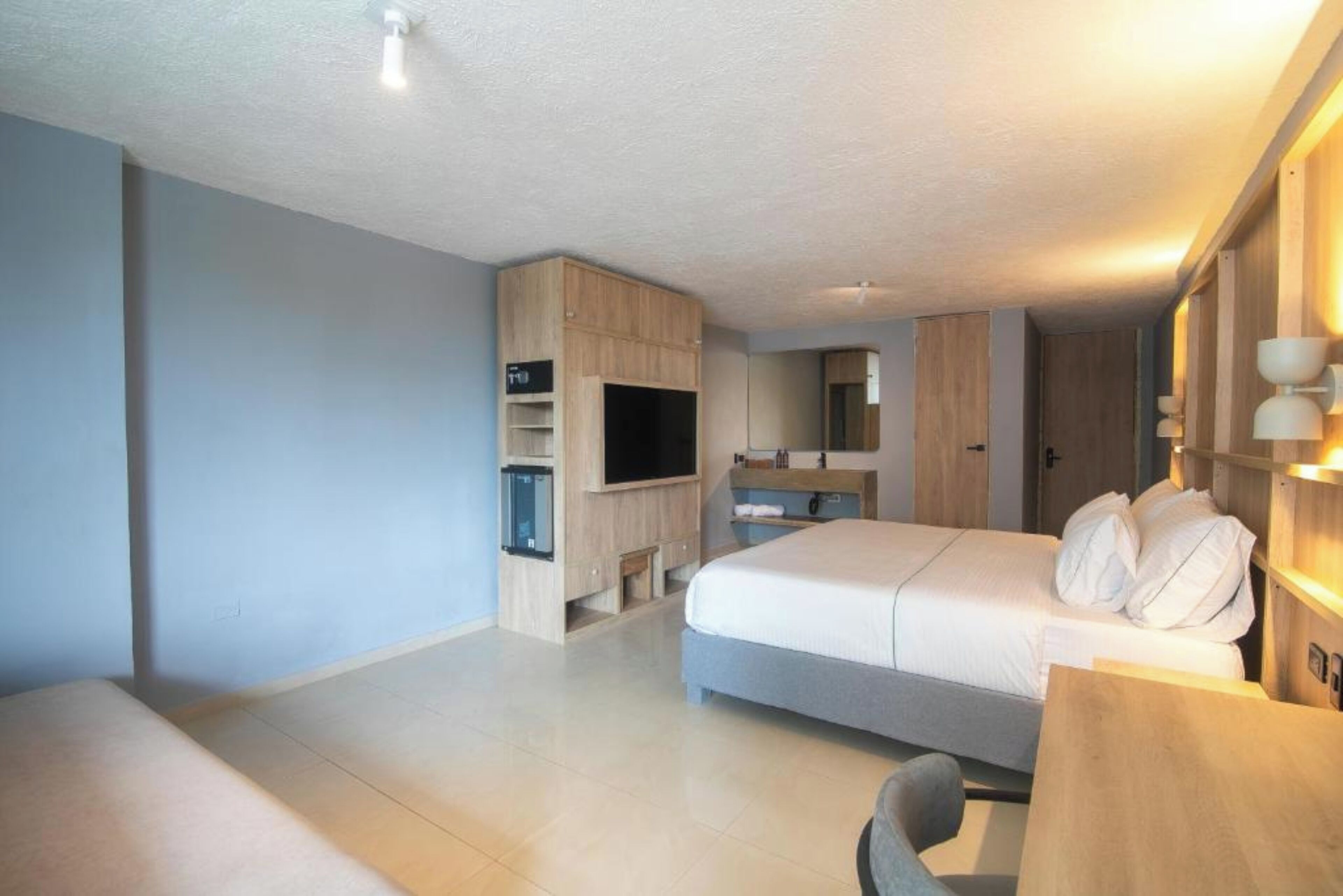 A modern hotel room with a large bed, a TV, a wooden cabinet, and a desk.