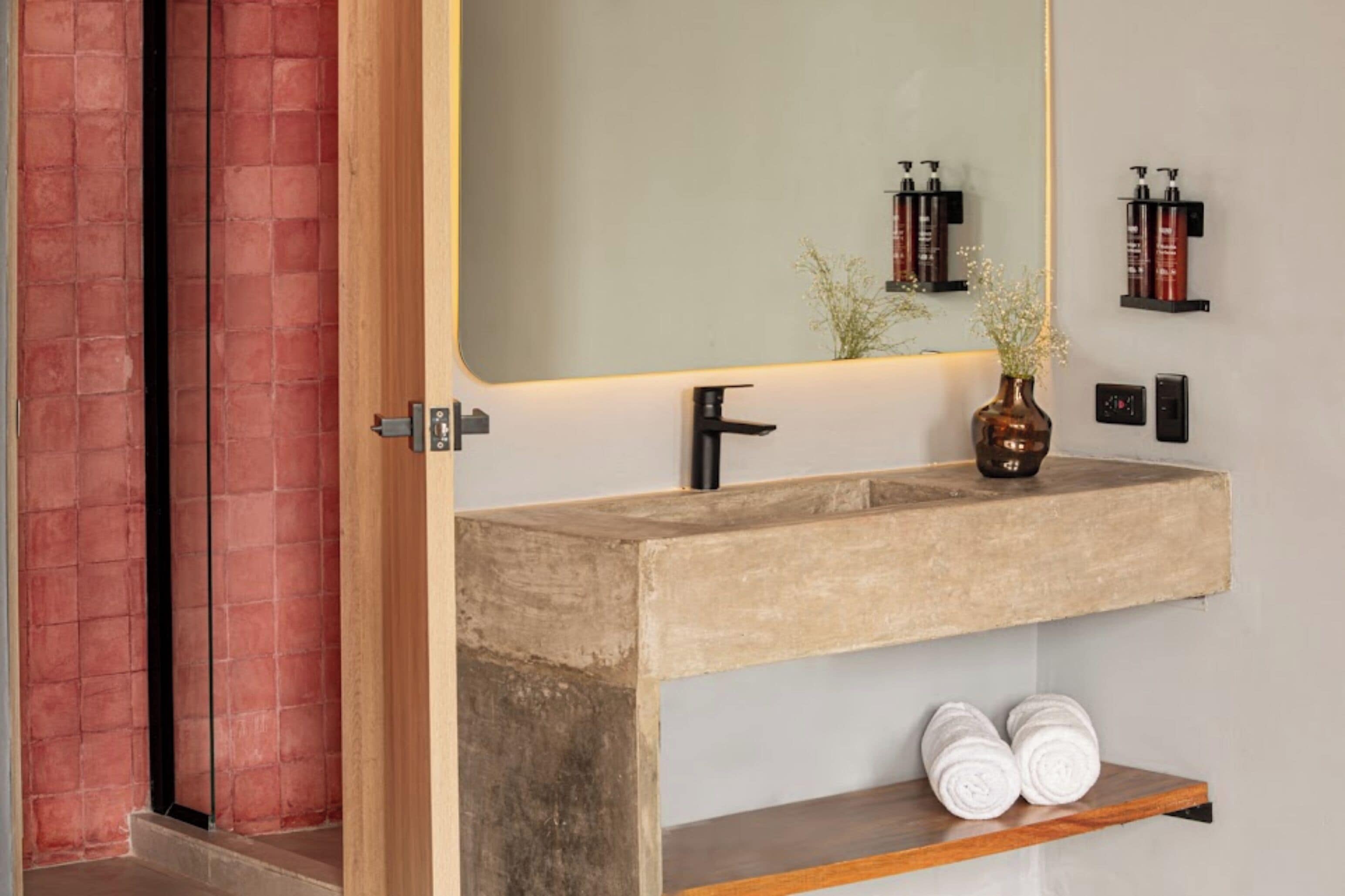 A bathroom with a concrete sink, a mirror, and a shelf with toiletries.