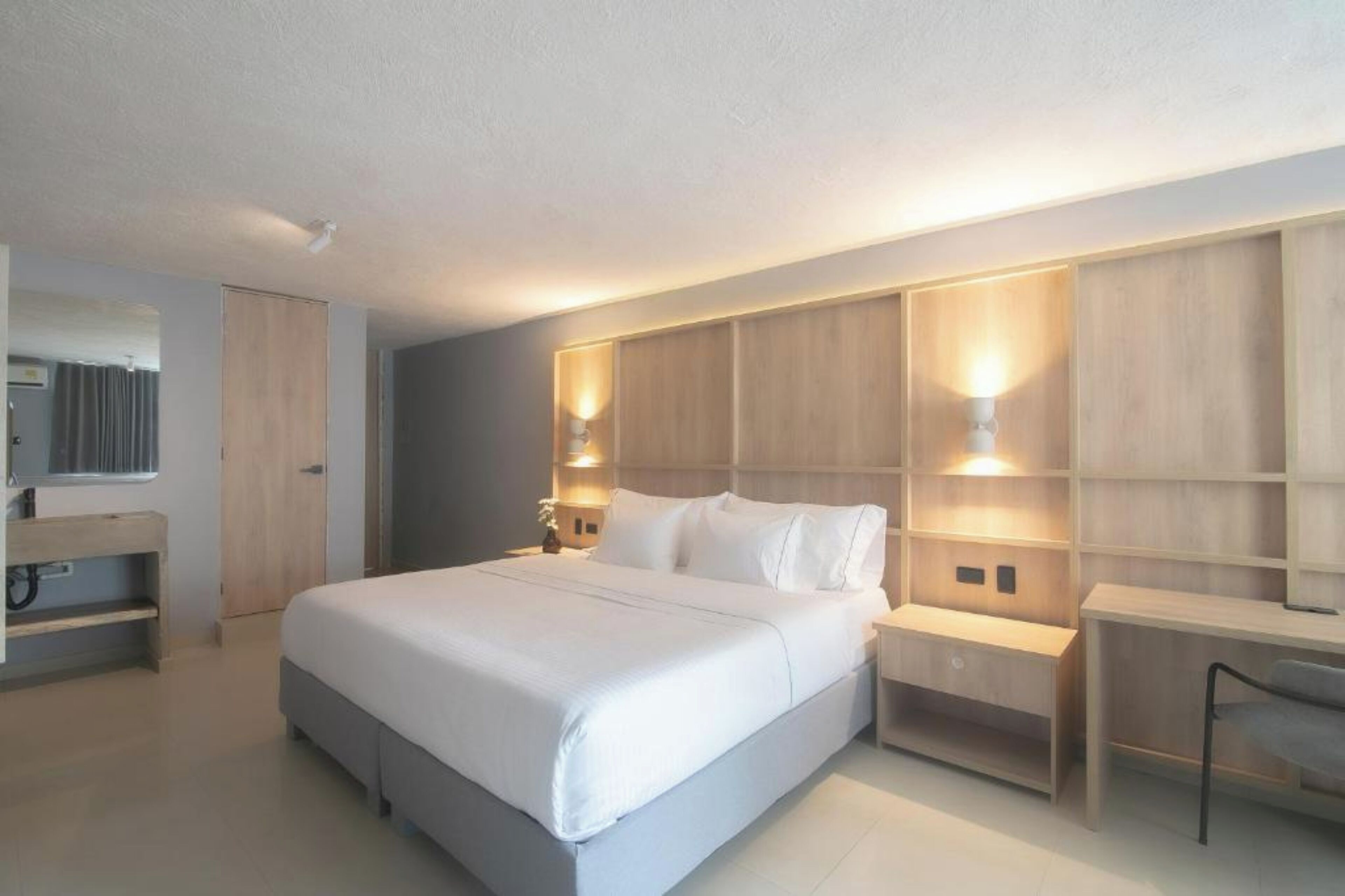 A modern bedroom with a large bed, bedside tables, a desk, and built-in shelving.