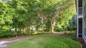 Un jardin bien entretenu, agrémenté de divers arbres et arbustes, un chemin de gravier et un bâtiment à l’extérieur blanc.