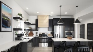 A modern kitchen with a central island, stainless steel appliances, black cabinetry, and pendant lighting. - Nine Lakefront Homes (sleeping 223) in Rocky Shores w/n 500ft (HOLLISTER)