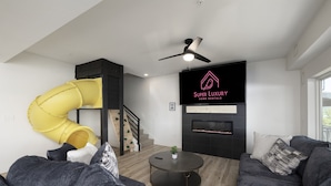 A modern living room with a sofa, a round coffee table, a fireplace, and a yellow slide. - Lakefront | Three homes (sleeps 68) golf simulators, outdoor saunas, & hot tubs (HOLLISTER)
