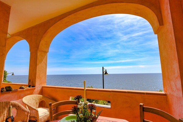 A balcony with wicker furniture and a table, overlooking the sea.