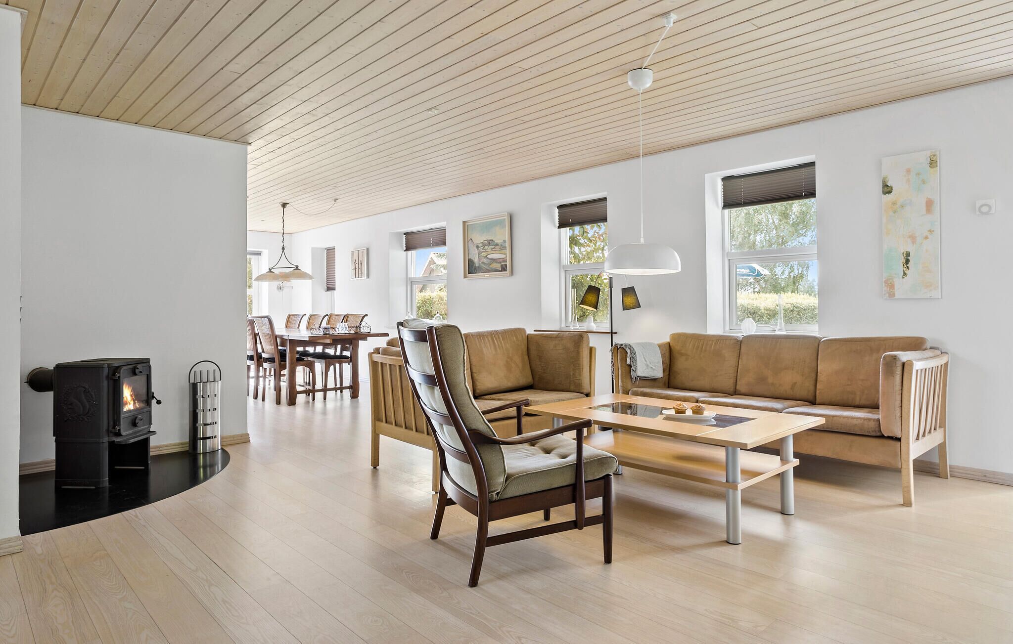 A spacious living room with a wooden ceiling, a fireplace, a dining area, and a sofa.
