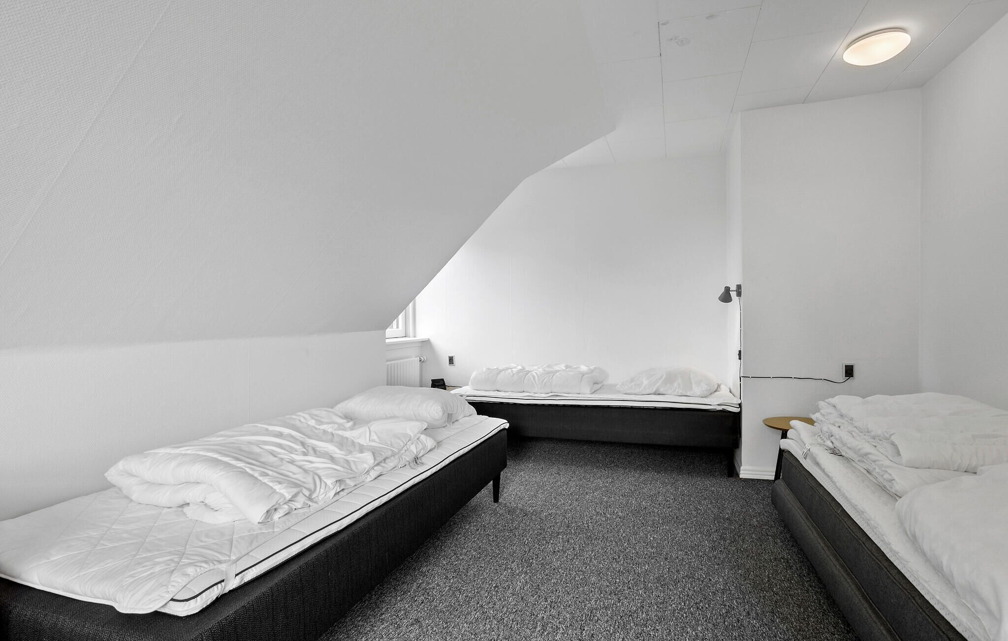 A small, white, single-room hotel with two beds, a carpeted floor, and a sloped ceiling.