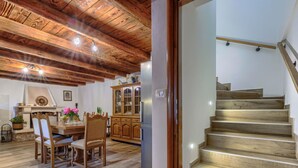 Un espace repas au sol en bois, avec une table et des chaises, un meuble avec des portes en verre et un escalier avec des marches en bois.