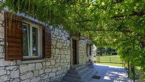 Un bâtiment en pierre avec des volets en bois, un escalier en pierre et une terrasse dallée.