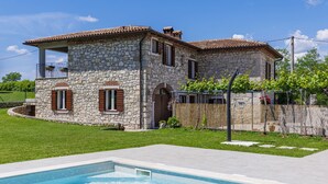 Une maison en pierre avec une piscine, un balcon et un jardin.