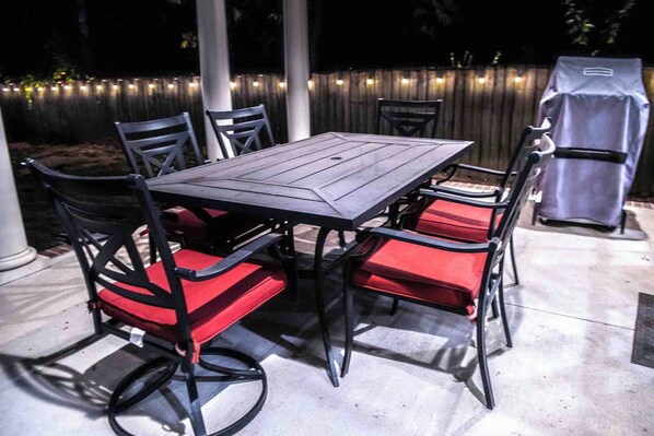 A covered patio with a table and chairs, a barbecue grill, and string lights.