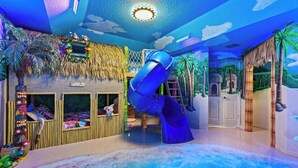 Una habitación con tobogán, literas y un mural de paisaje tropical.
