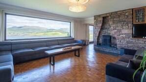 A living room with a stone fireplace, a large window with a view of hills, and a sofa. - Dingle Bay Nest Burnham (Ventry)