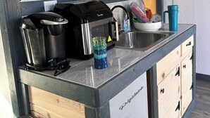Ett kompakt kök med en kaffebryggare, en vattenkokare, ett handfat och en blå vattenflaska.
