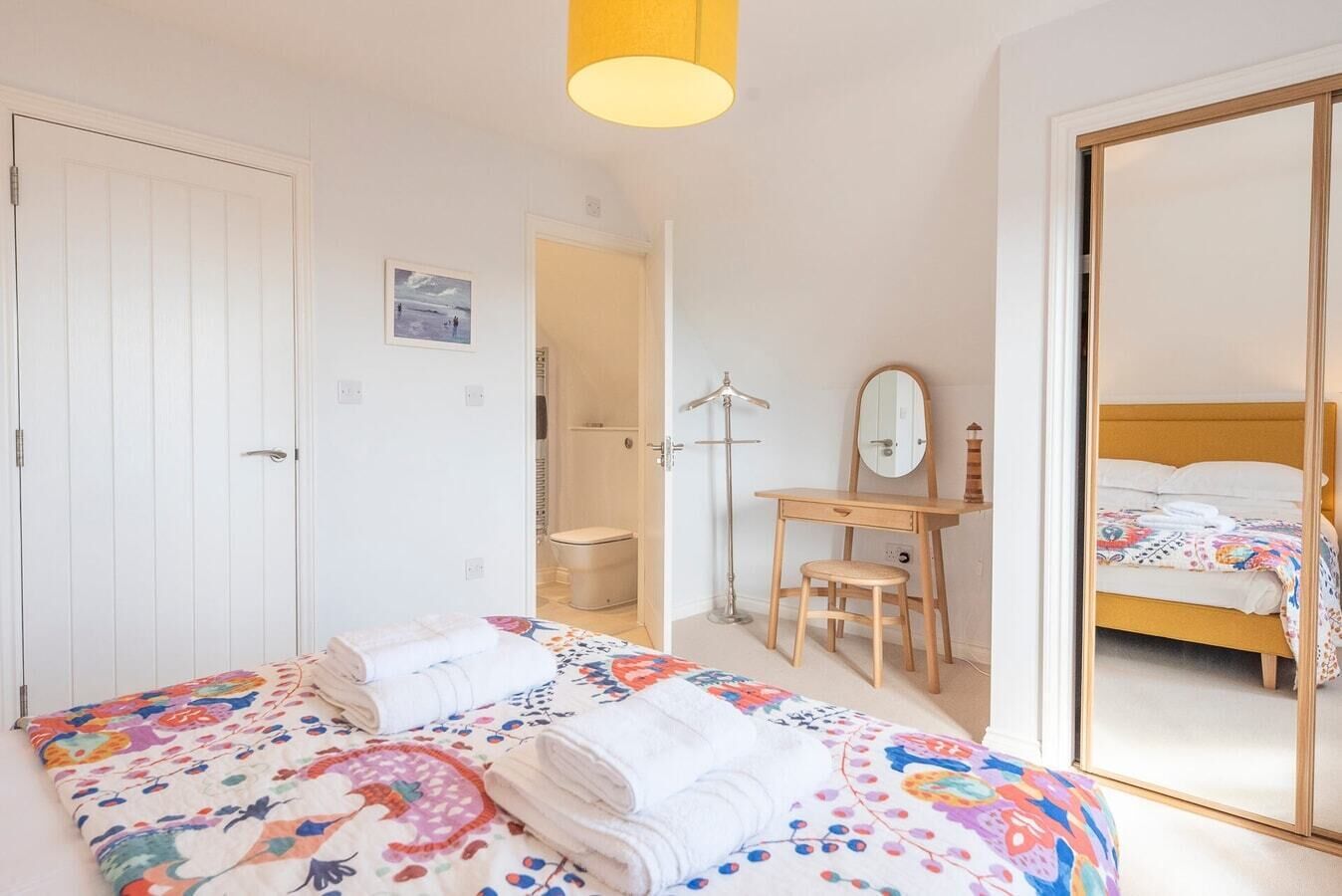 A bedroom with a bed, a desk, a mirror, and a wardrobe.