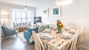 A dining area with a table set for four, a sofa, and a television in the background. - The Salty Dog, Aldeburgh (Suffolk)