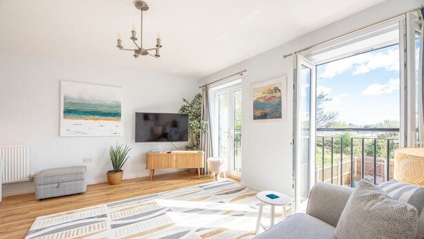 A spacious living room with a large sofa, a TV, a wooden cabinet, and a balcony with a view. - The Salty Dog, Aldeburgh (Suffolk)