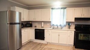 A modern kitchen with white cabinets, stainless steel appliances, and a wooden floor. - Cozy and Quiet Lafayette Home 2 (Lafayette Parish)