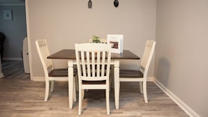 A dining area with a wooden table and four white chairs. A welcome sign is placed on the table. - Cozy and Quiet Lafayette Home 2 (Lafayette Parish)