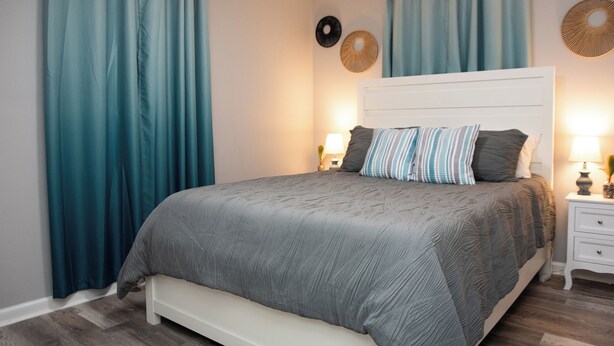 A bedroom with a bed, curtains, and wall decor. - Cozy and Quiet Lafayette Home 2 (Lafayette Parish)