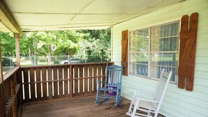 A covered porch with a wooden railing, a rocking chair, and a blue chair. - Cozy and Quiet Lafayette Home 2 (Lafayette Parish)