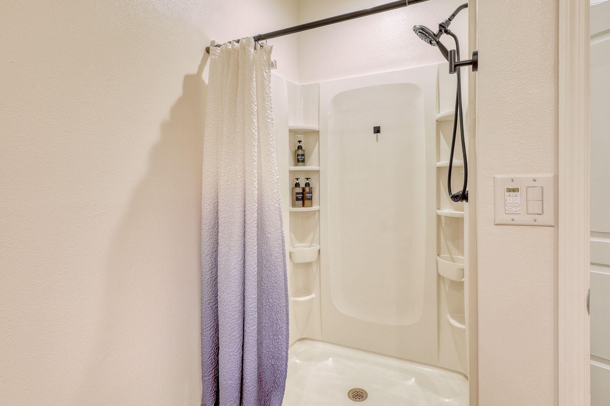 A shower area with a white bathtub, a showerhead, and a control panel.
