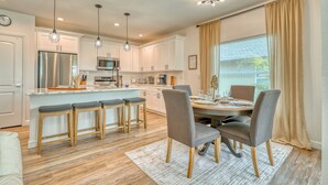 A modern kitchen with a central island, bar stools, and a dining area with a table and chairs.