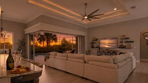 Una sala de estar moderna con un sofá grande, un comedor con mesa de vidrio y vistas a un atardecer a través de grandes ventanales.
