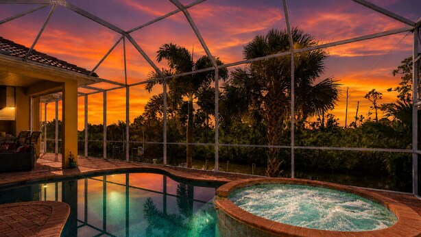 Piscina con hidromasaje, sillas de descanso y vistas a palmeras y al atardecer.