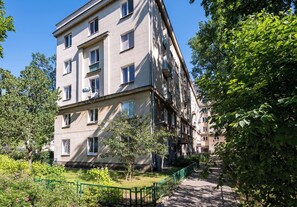 A multi-story residential building with balconies, a green fence, and trees in the courtyard.