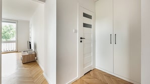 A room with a wooden herringbone floor, white walls, a white wardrobe with two doors, and a small wooden desk with a laptop. - Nowa Praga Standard Apartment (Warszawa)