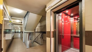 A corridor with a red elevator, a staircase, and a security camera on the wall. - Nowa Praga Standard Apartment (Warszawa)