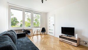A modern living room with a large window, a sofa, a TV, and a small table with chairs. - Nowa Praga Standard Apartment (Warszawa)