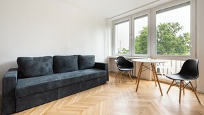 A modern living room with a sofa, two chairs, a small table, and large windows. - Nowa Praga Standard Apartment (Warszawa)