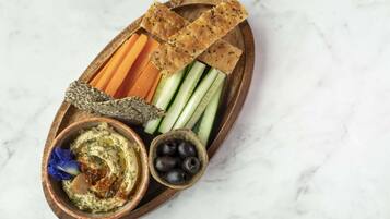 A wooden tray with hummus, olives, carrots, cucumbers, and crackers.