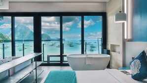Un baño moderno con una bañera grande, un banco y vista a barcos en un mar tranquilo.