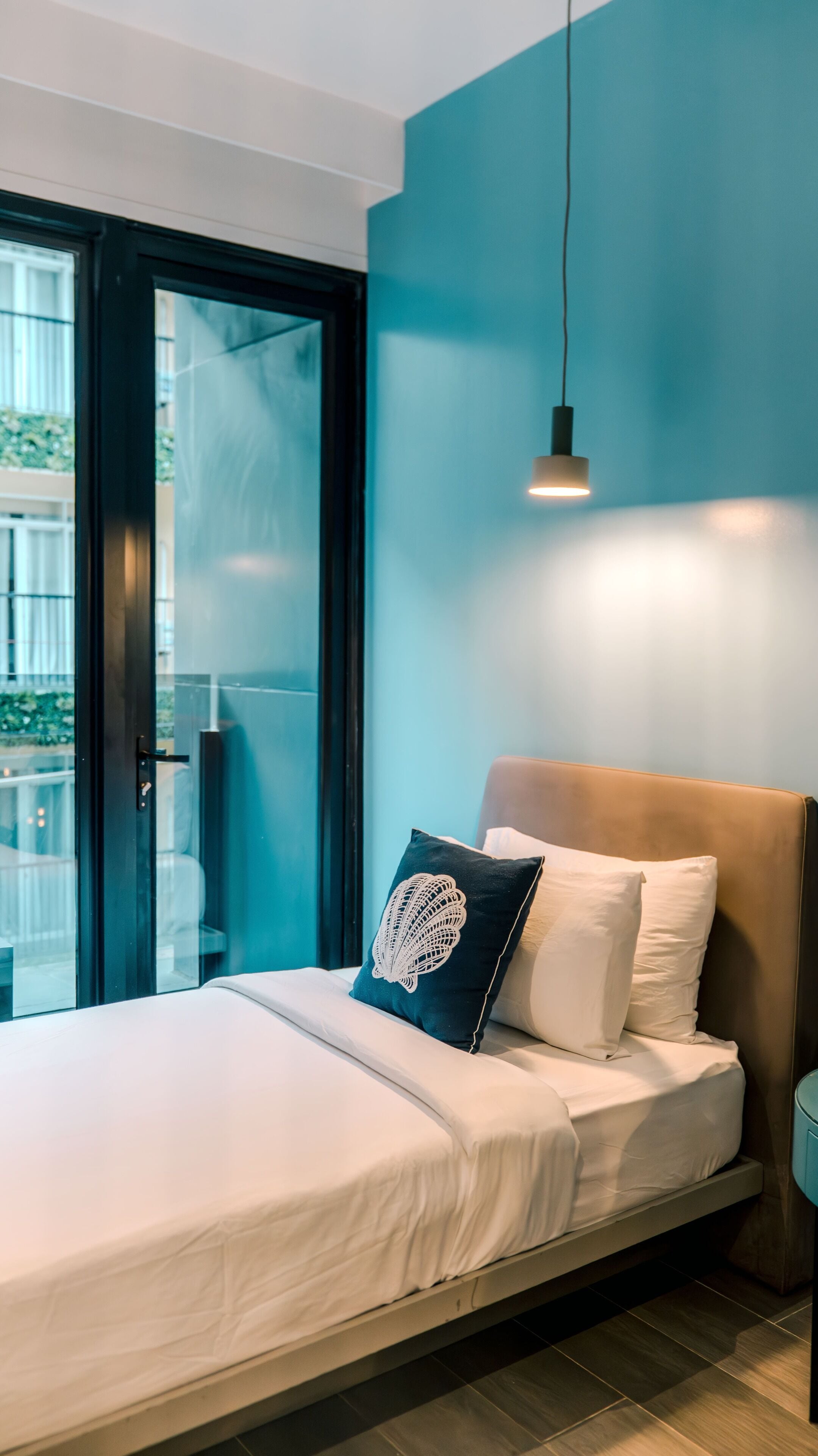 A bedroom with a bed, pillows, a hanging light, and a view through a glass door.
