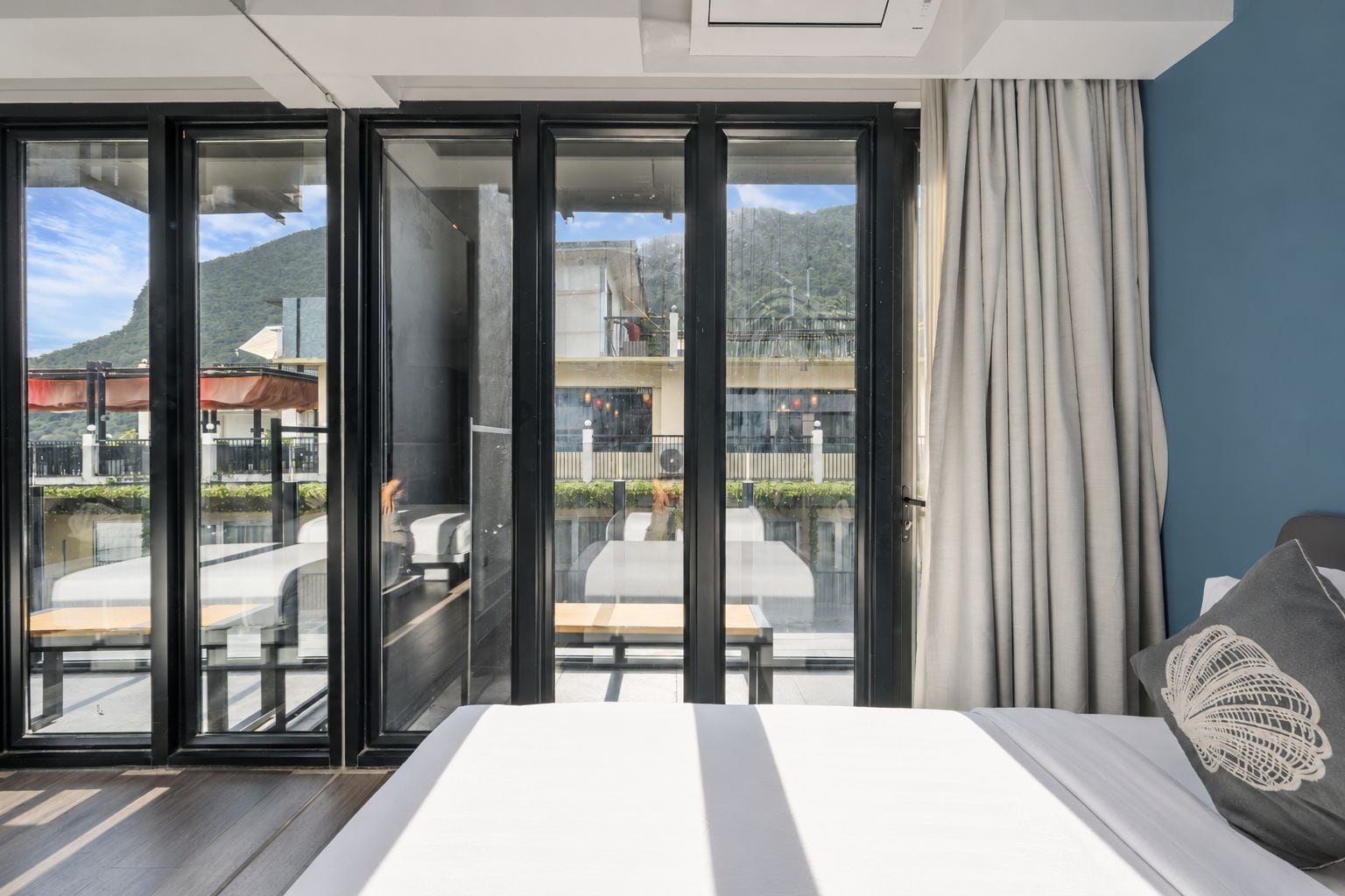 A hotel room with a bed, a view through glass doors to an outdoor seating area, and a curtain on the window.