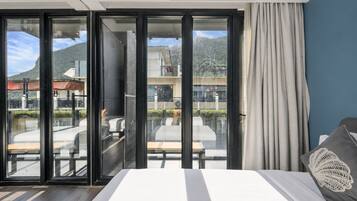 Habitación de hotel con una cama, vistas a un área exterior con mesas y sillas a través de puertas de vidrio, y una cortina en la ventana.