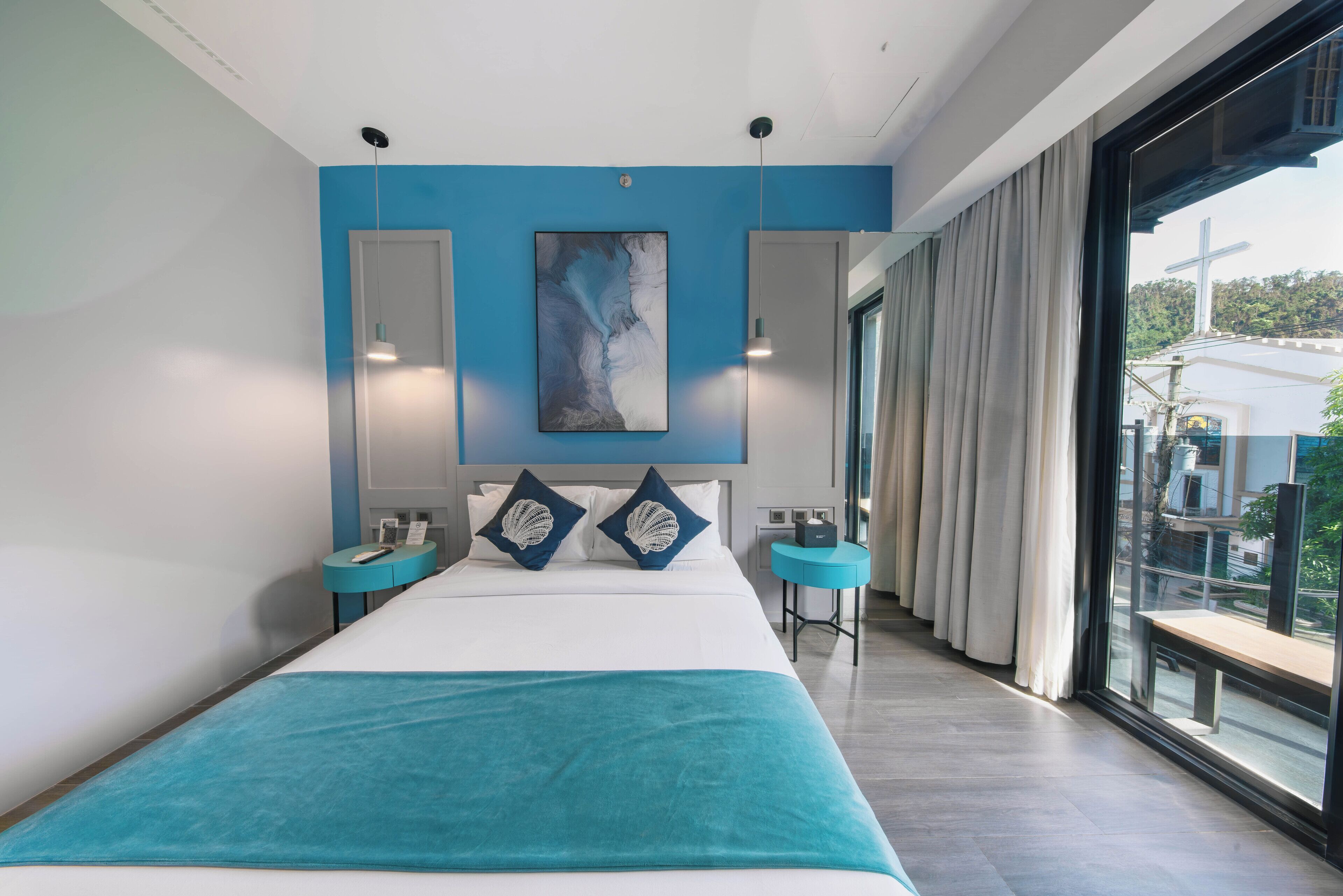 A modern hotel room with a large bed, a view of the city, and a balcony with a cross.