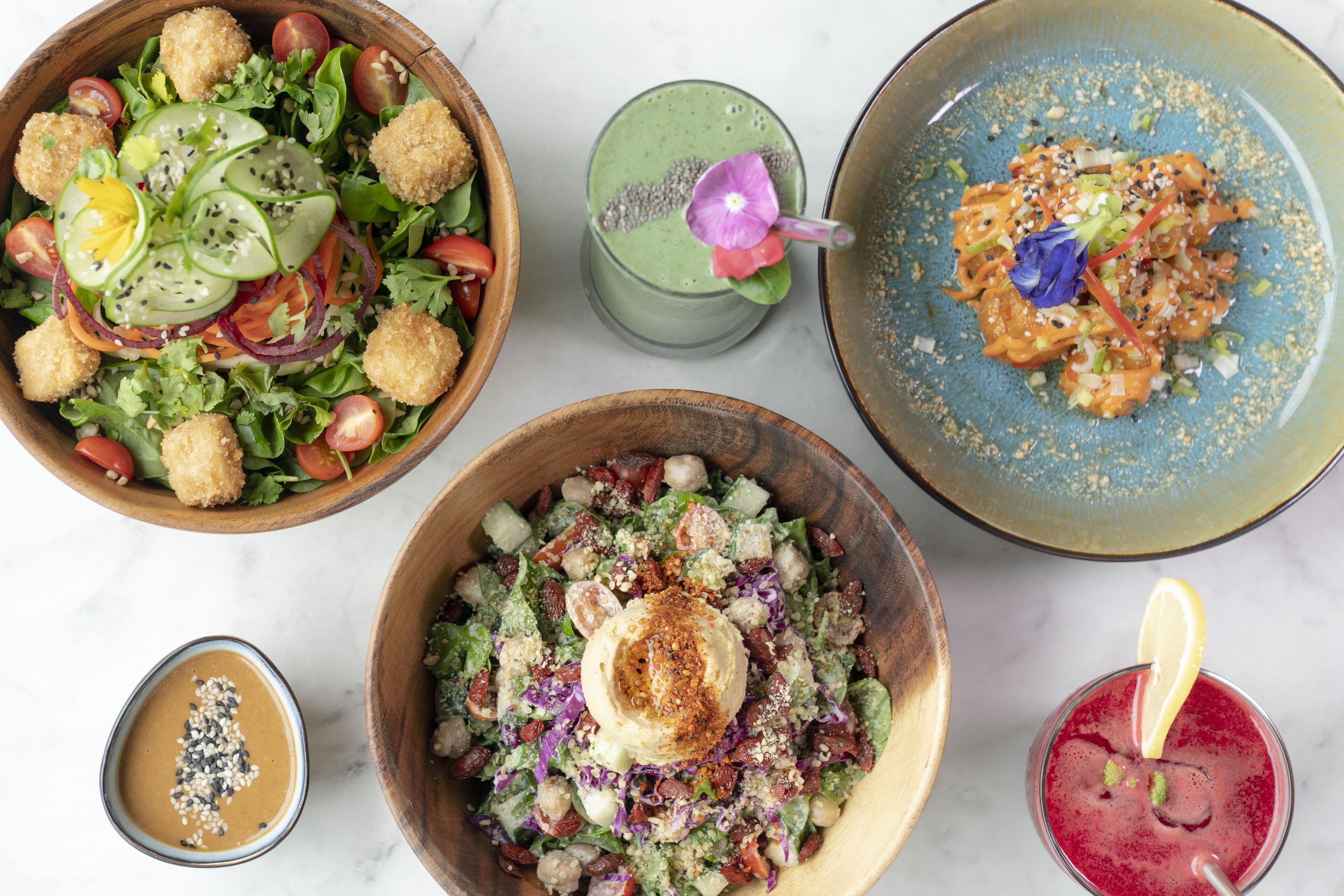 A variety of dishes including a salad, a green smoothie, and a bowl of food with a dollop of sauce.