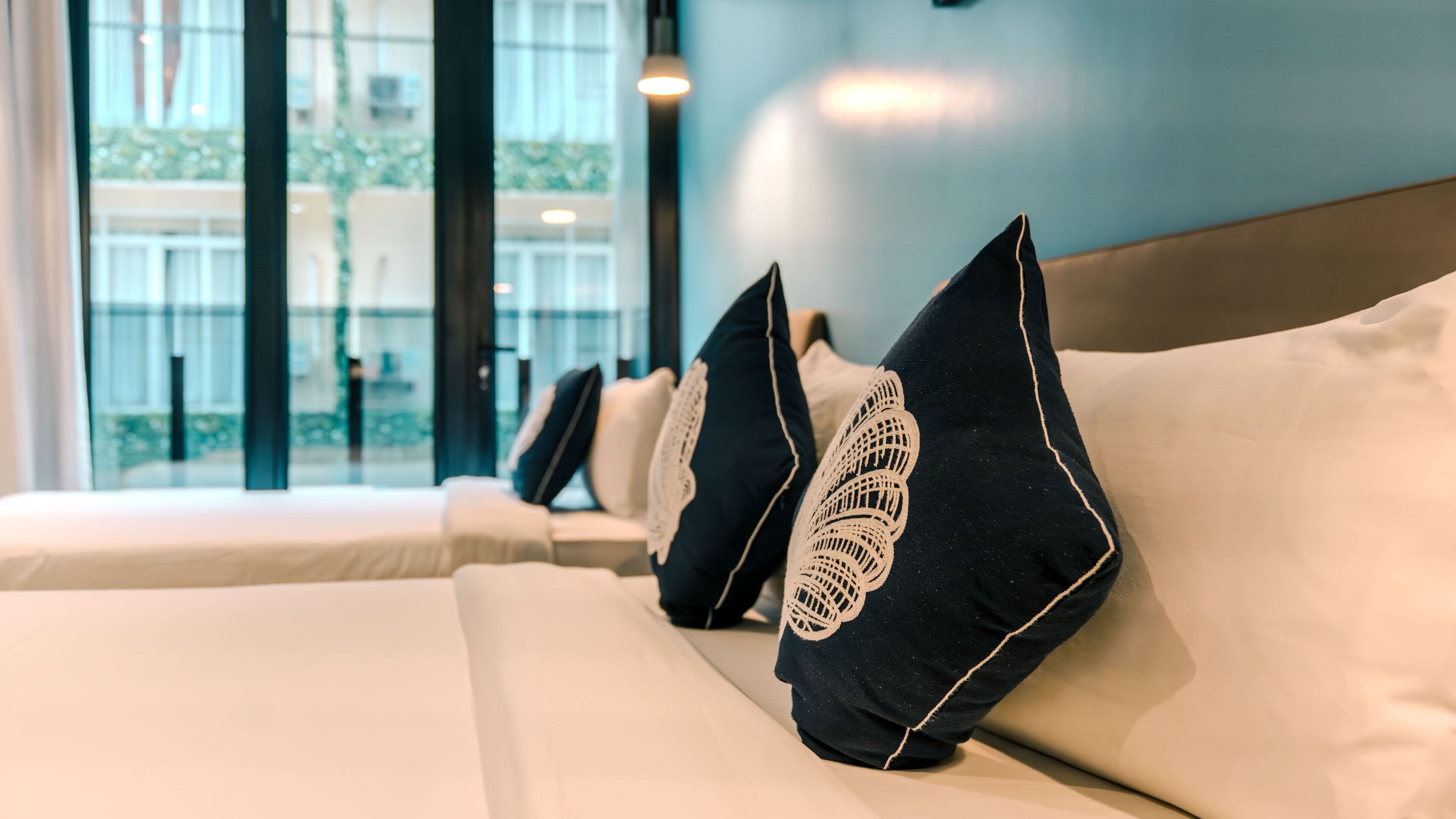 Habitación de hotel con una fila de camas, cada una con un colchón blanco y almohada negra con un diseño bordado en blanco.