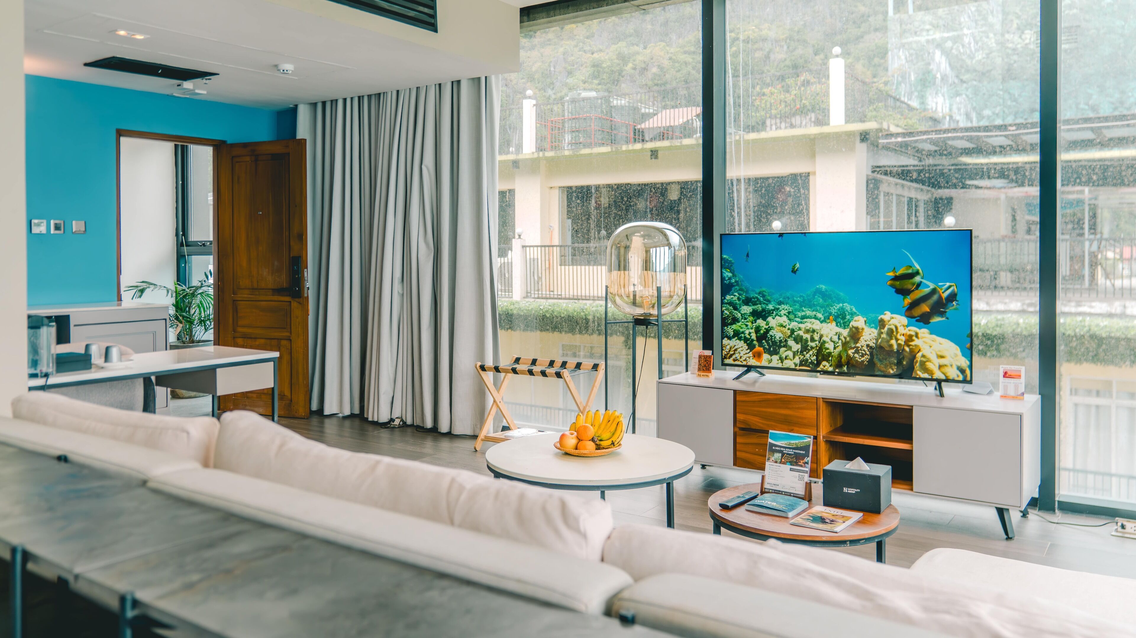 A modern living room with a large TV, a sofa, a coffee table, and a view of a balcony.