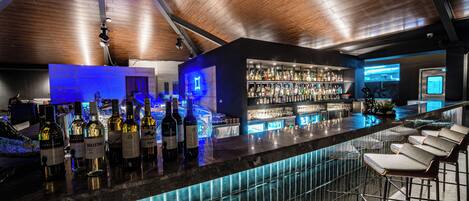 A bar with a wooden ceiling, a bar counter with bottles, and bar stools.