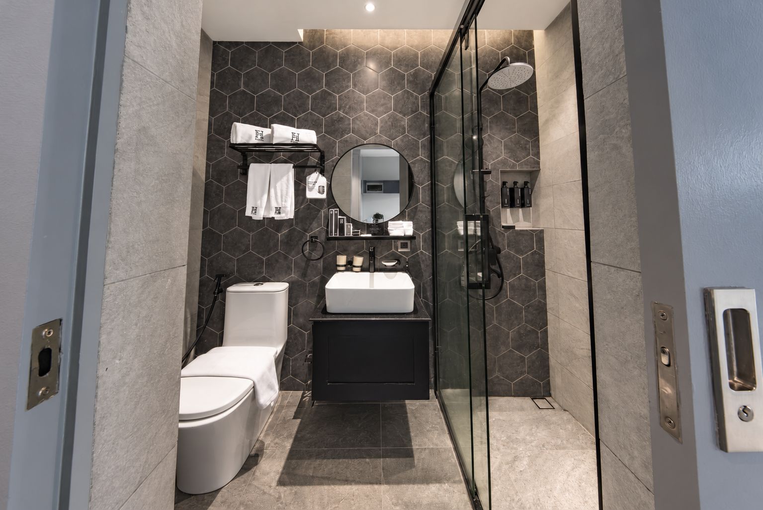 A modern bathroom with a glass shower enclosure, a white toilet, a black vanity, and a hexagonal tile backsplash.