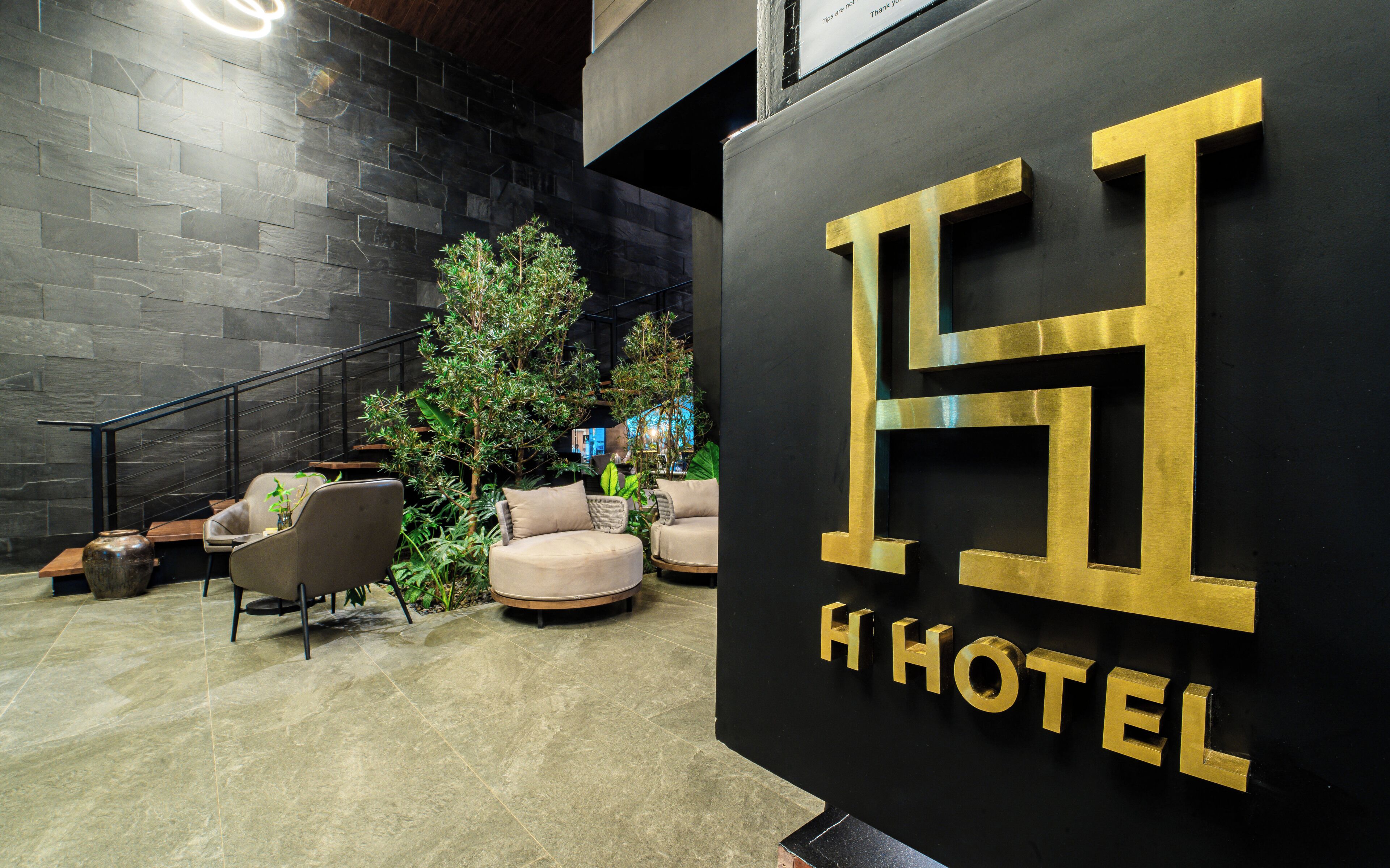 A modern hotel lobby with a stone wall, a staircase, and comfortable seating areas.