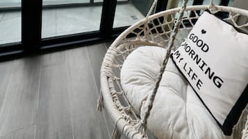 A room with a large window, a hanging chair with a cushion, and a view of greenery and buildings.