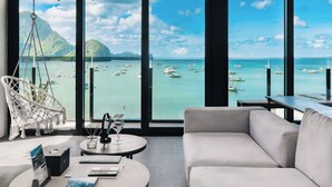 Una habitación con un ventanal grande, un sillón colgante, un sofá, una mesita con un vaso y una computadora portátil.