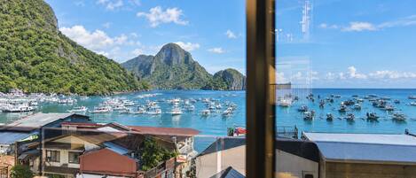 Un pueblo costero con barcos amarrados, montañas al fondo y edificios con señalización visible.