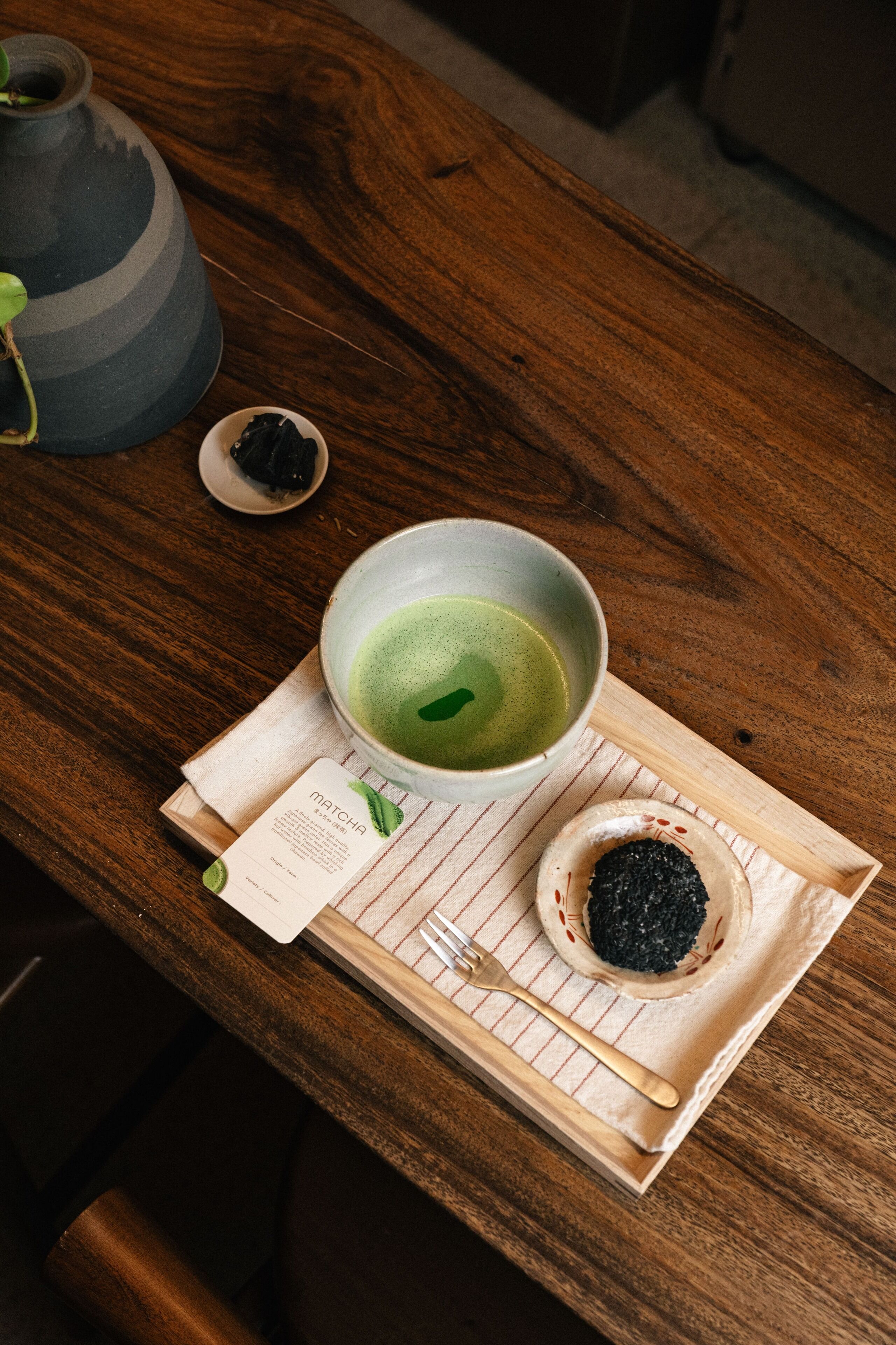 A wooden table with a bowl of matcha, a small dish of matcha powder, and a menu.
