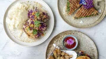 Three plates of food with different dishes, including a salad, grilled sandwich, and fried potatoes.
