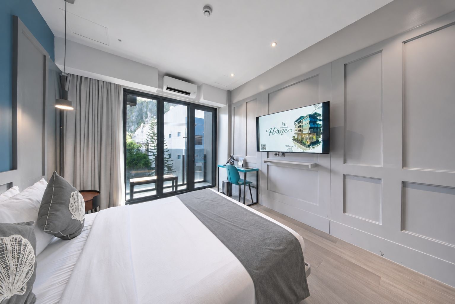 Une chambre d’hôtel moderne dotée d’un grand lit, d’un bureau, d’un téléviseur à écran plat et d’une porte-fenêtre coulissante donnant sur l’extérieur.